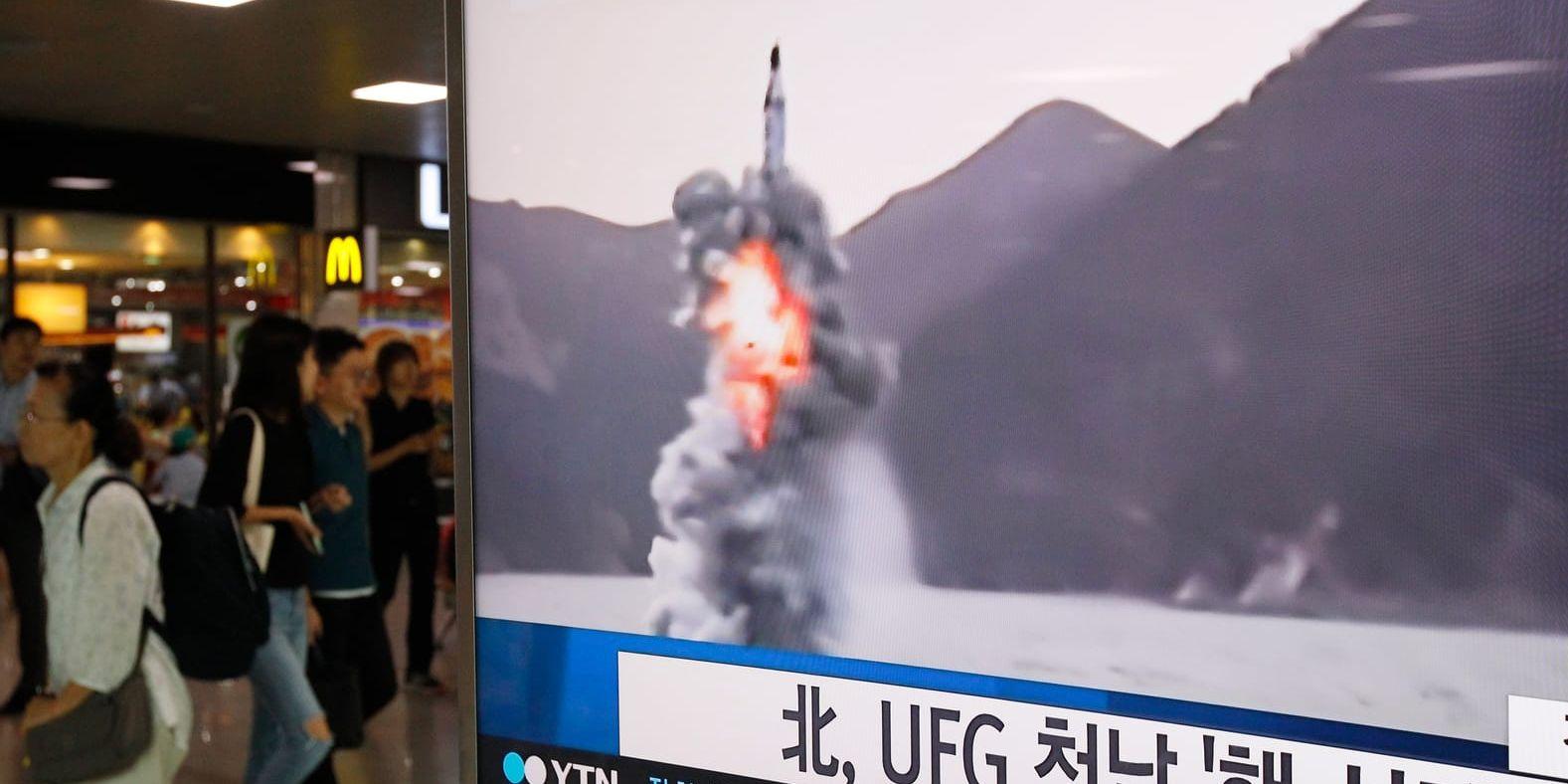 Människor passerar ett nyhetsinslag på tv om robotuppskjutningen, med arkivbilder från tidigare testskjutningar från Nordkorea. Rubriken lyder "Nordkorea skjuter upp robot under UFG (militärövningen med USA)".
