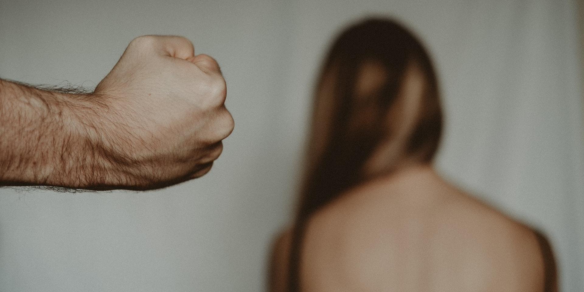 misshandel - en knuten näve, kvinna i bakgrunden - genrebild