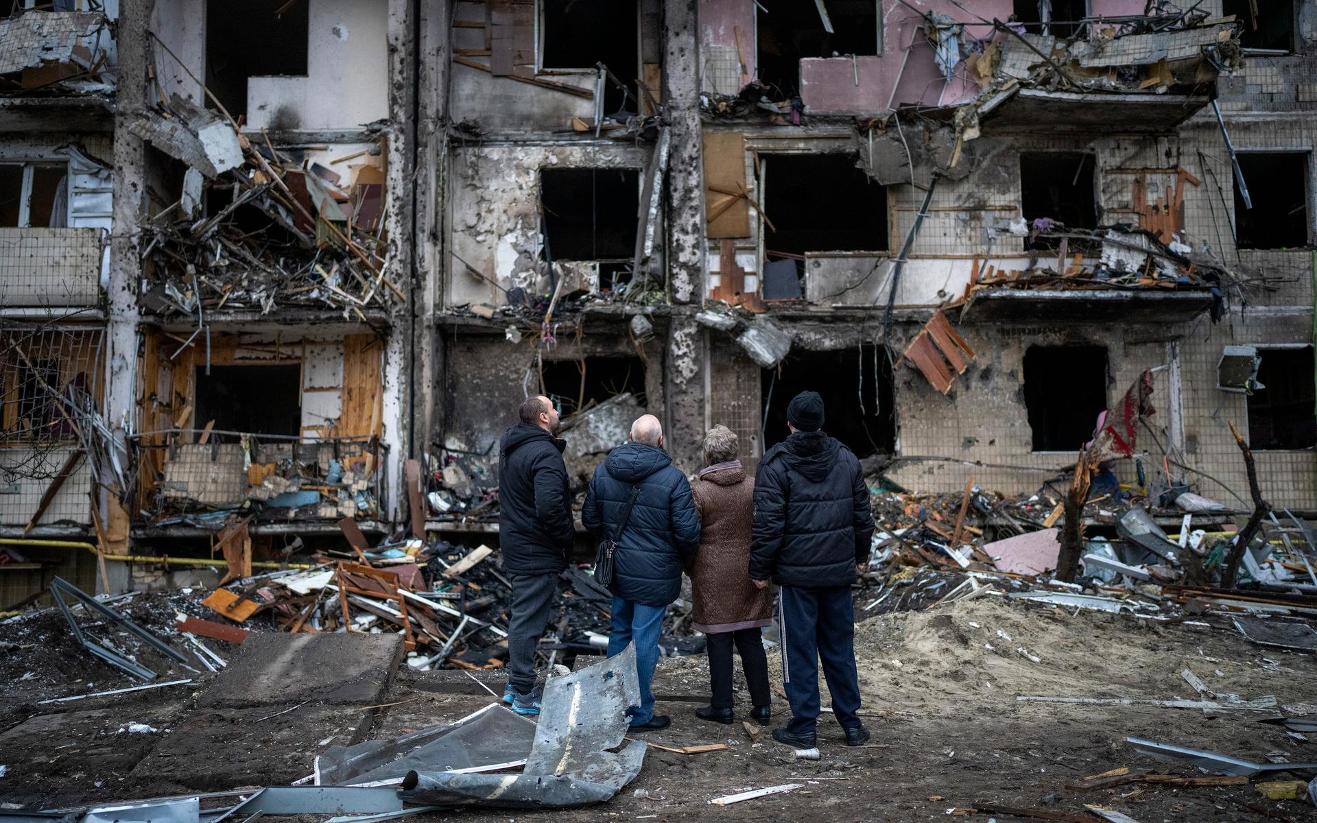 Fler invånare i Kiev står och blickar utöver ett bostadshus som under den tidiga fredagsmorgonen utsatts för en raketattack.