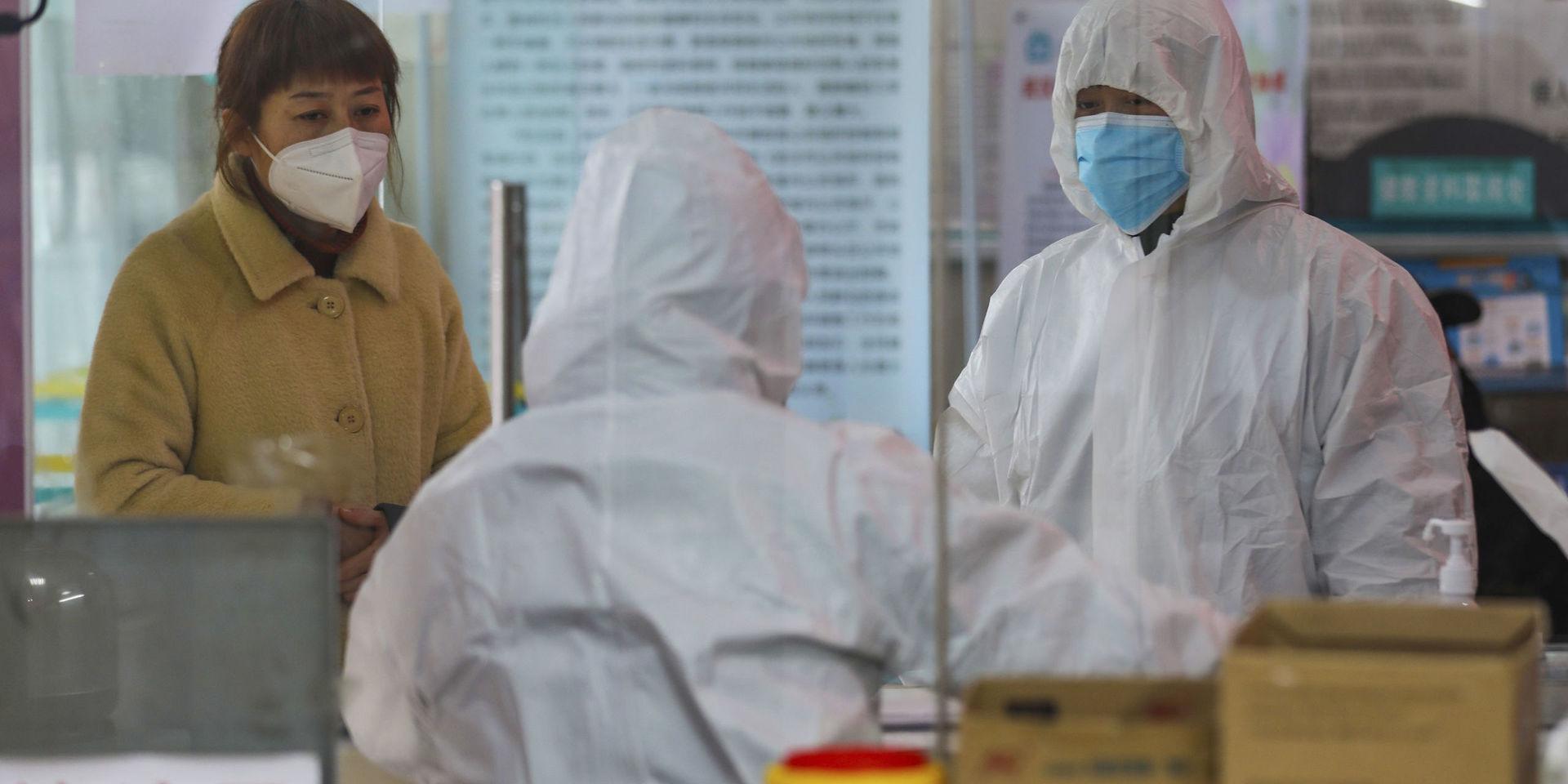 Vårdpersonal i skyddskläder talar med en kvinna som söker vård med symtom på coronavirus vid en läkarstation i Wuhan i Kina.