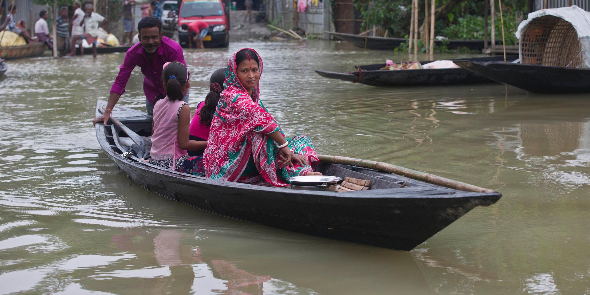 En familj försöker ta sig över en översvämmad väg i byn Burha Burhi i Assam i Indien.