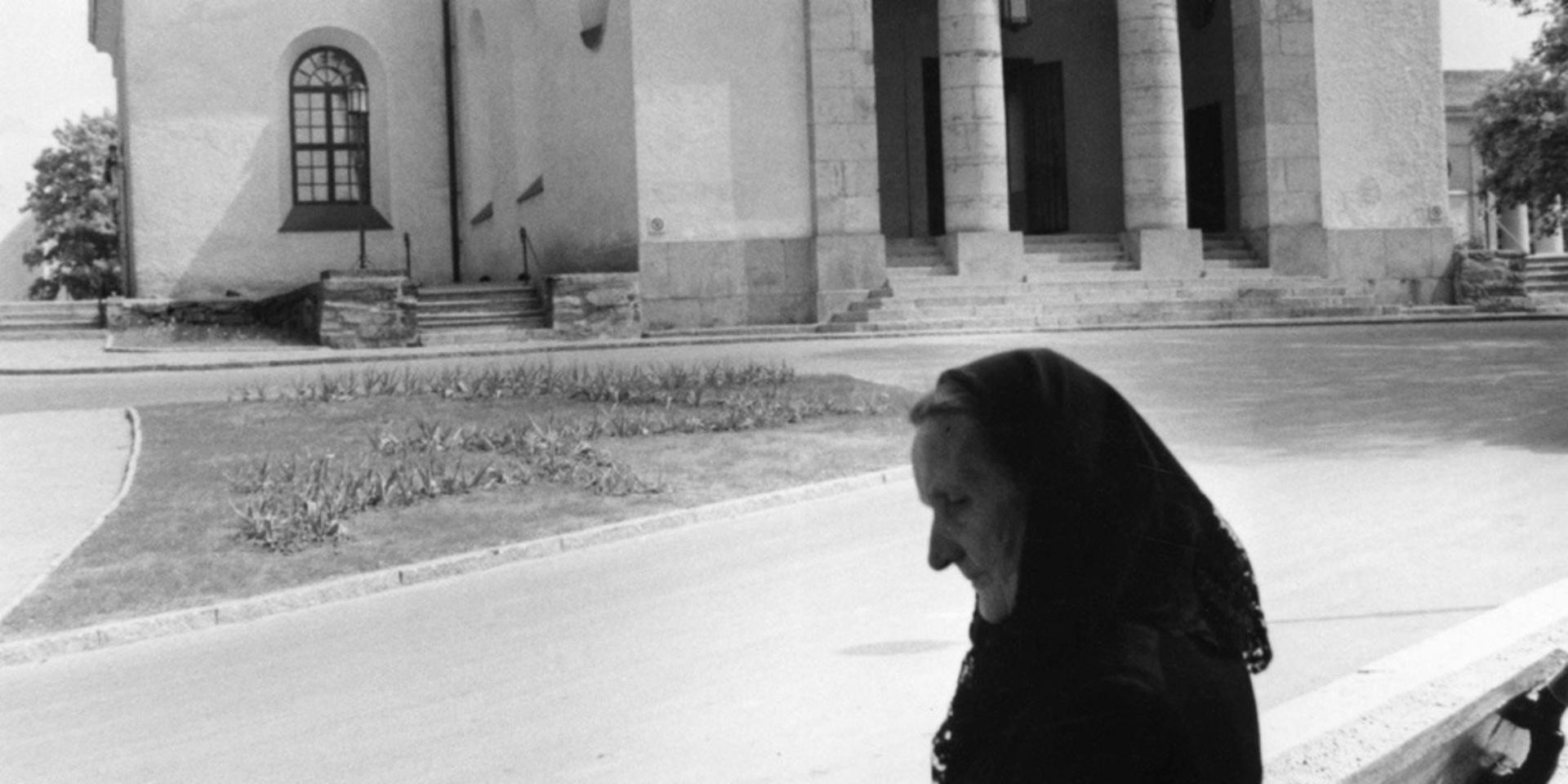 En gammal kvinna sitter på en bänk framför Uddevalla kyrka år 1956.