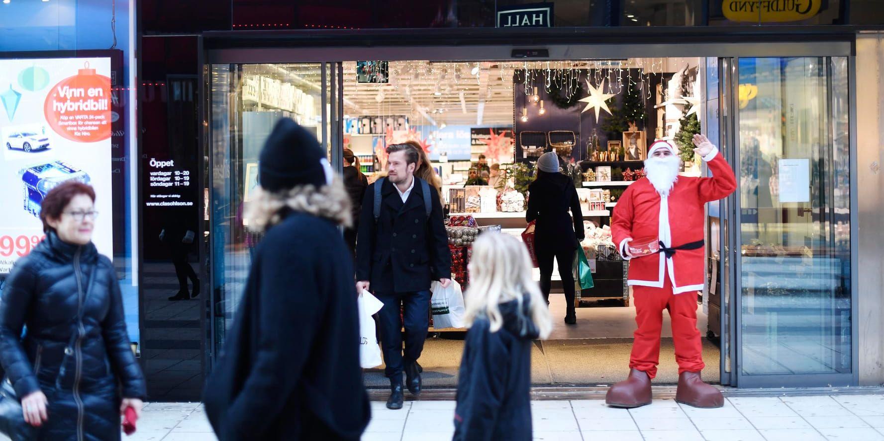 En tomte utanför en julaftonsöppen butik i centrala Stockholm bjuder på pepparkakor och önskar förbipasserande god jul.