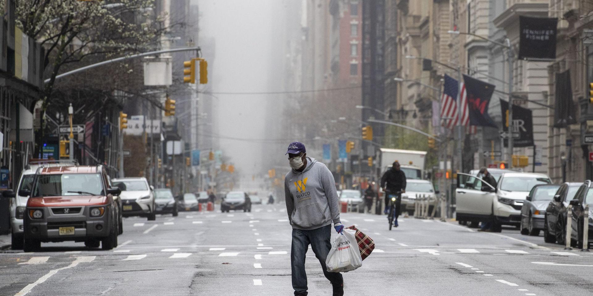 En man med munskydd korsar femte avenyn i New York.