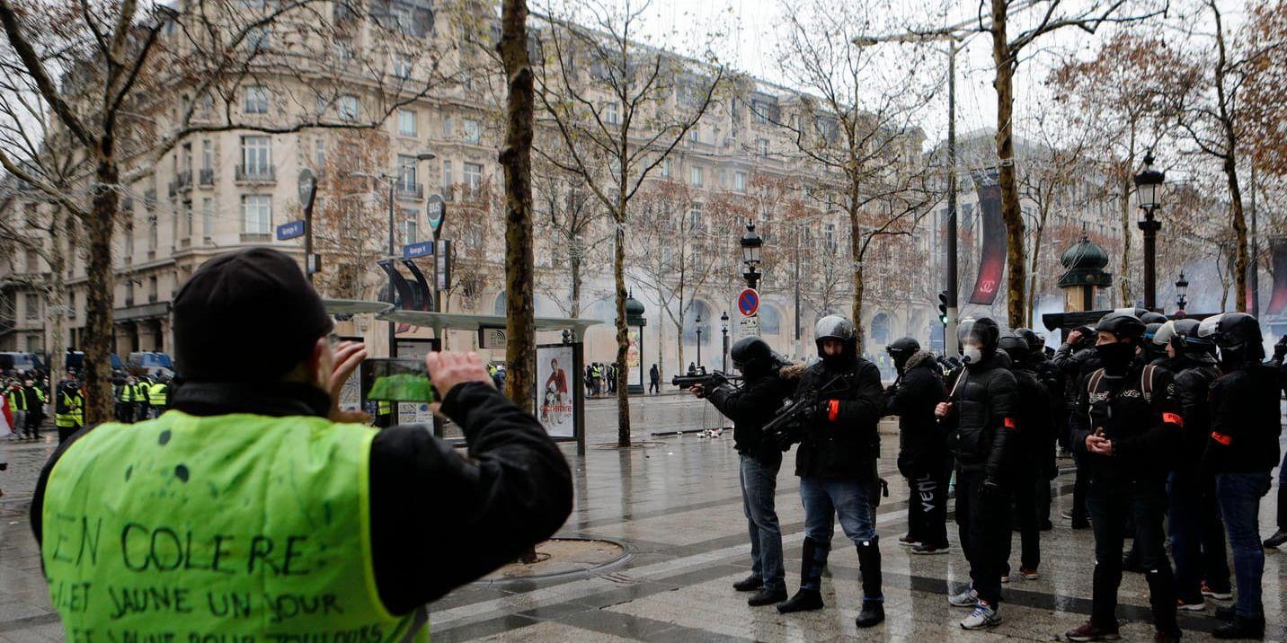 En demonstrant från proteströrelsen Gula västarna tar en bild av kravallpoliser på paradgatan Champs-Élysées i Paris på lördagen.