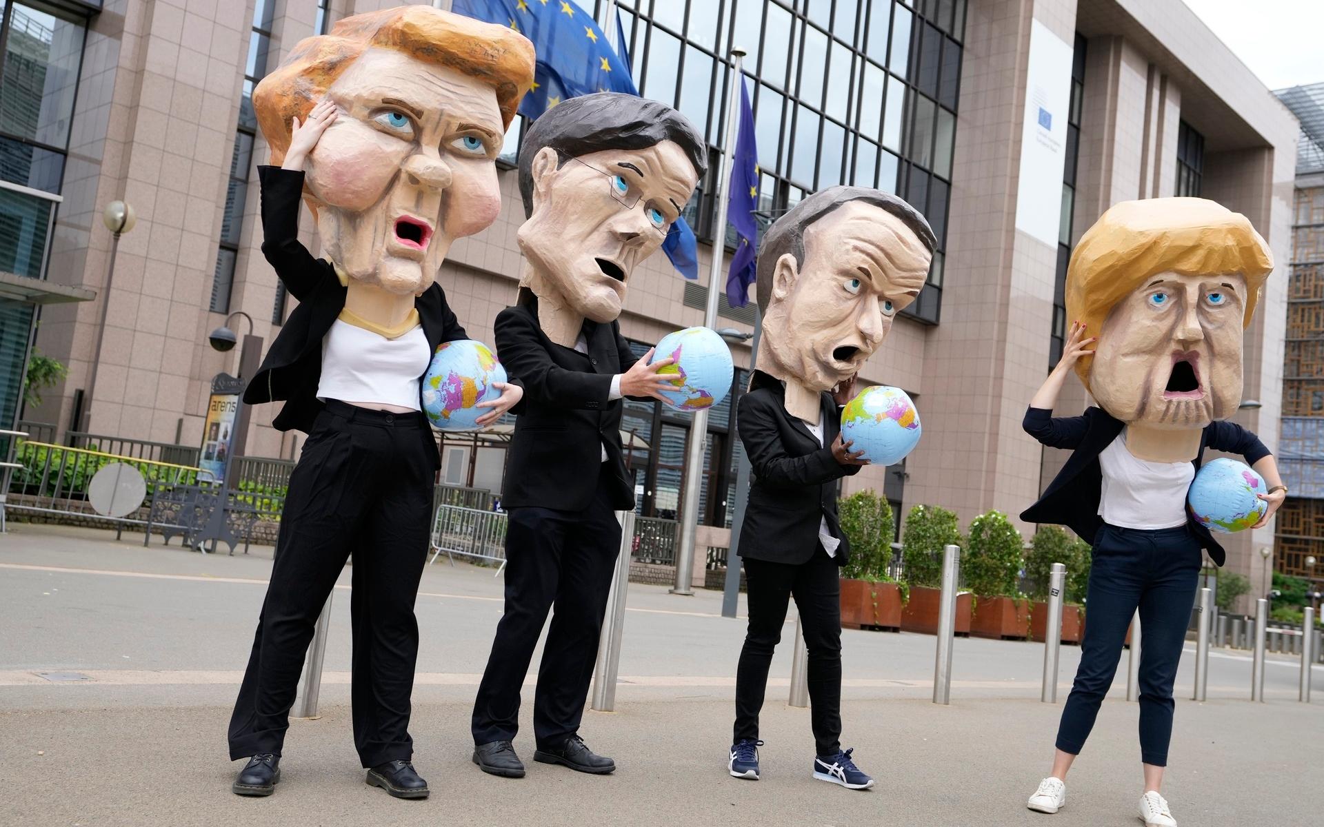Climate activists wearing giant heads depicting EU leaders, from left to right, European Commission President Ursula von der Leyen, German Chancellor Angela Merkel, Dutch Prime Minister Mark Rutte and French President Emmanuel Macron hold globes as they demonstrate in front of the European Council building in Brussels, Tuesday, July 6, 2021. The demonstration was held to highlight the threat of the Energy Charter Treaty (ECT) to climate action. (AP Photo/Virginia Mayo)  VLM104