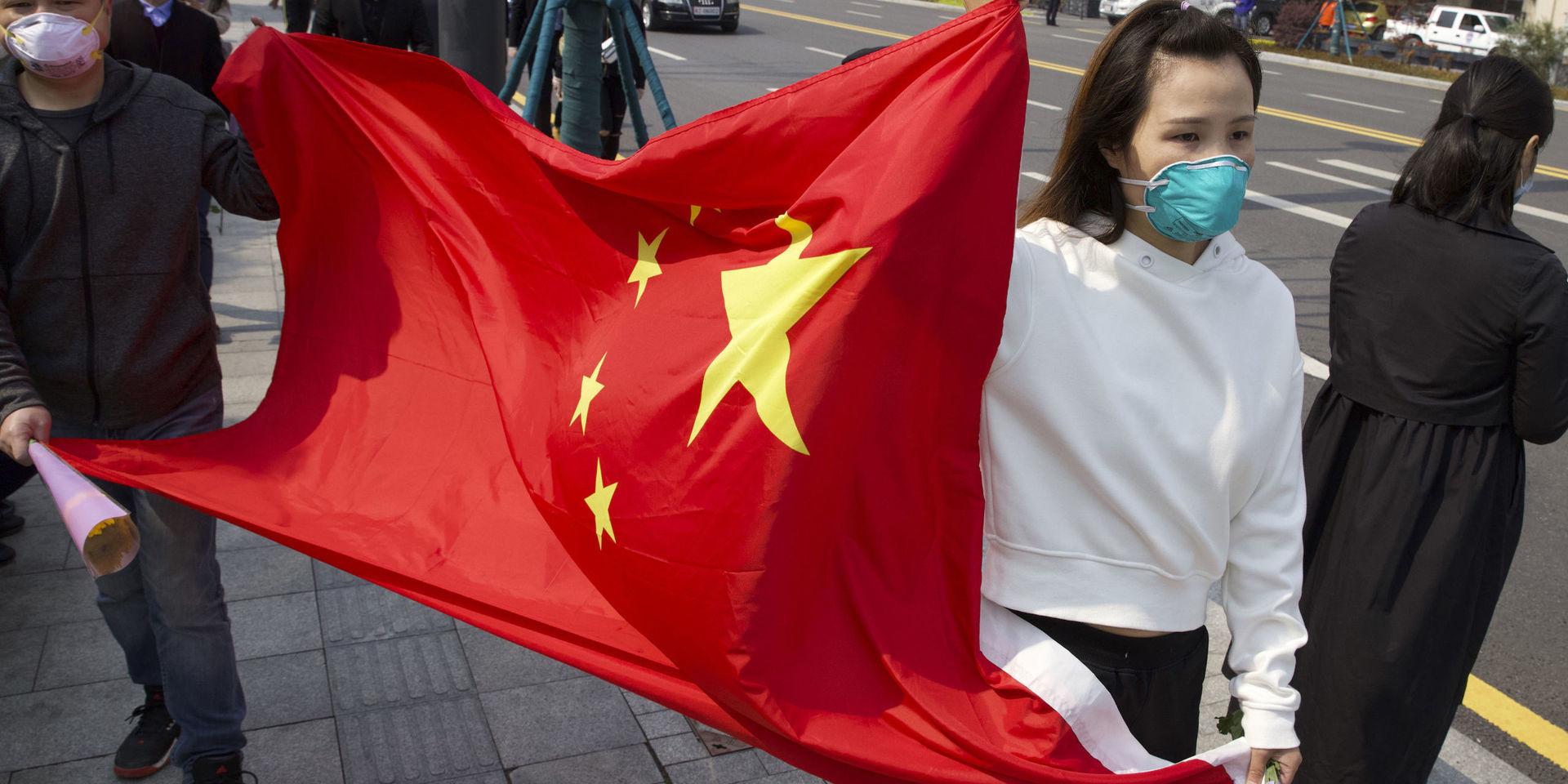 People hold a Chinese flag as they gather outside of a park where an official memorial was held for victims of coronavirus in Wuhan in central China&apos;s Hubei Province, Saturday, April 4, 2020. With air raid sirens wailing and flags at half-mast, China held a three-minute nationwide moment of reflection to honor those who have died in the coronavirus outbreak. (AP Photo/Ng Han Guan)  XHG215