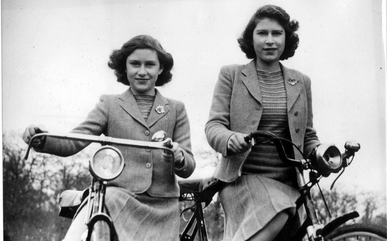 Prinsessorna Elizabeth och Margareth. På cykeltur  vid slottet i Windsor. Likadant klädda i randig jumper under dräkt med veckad kjol. Liten brosch på jackslaget. Vi ser den framtida drottningen Elizabeth till höger i bild. Bilden är från april 1942.