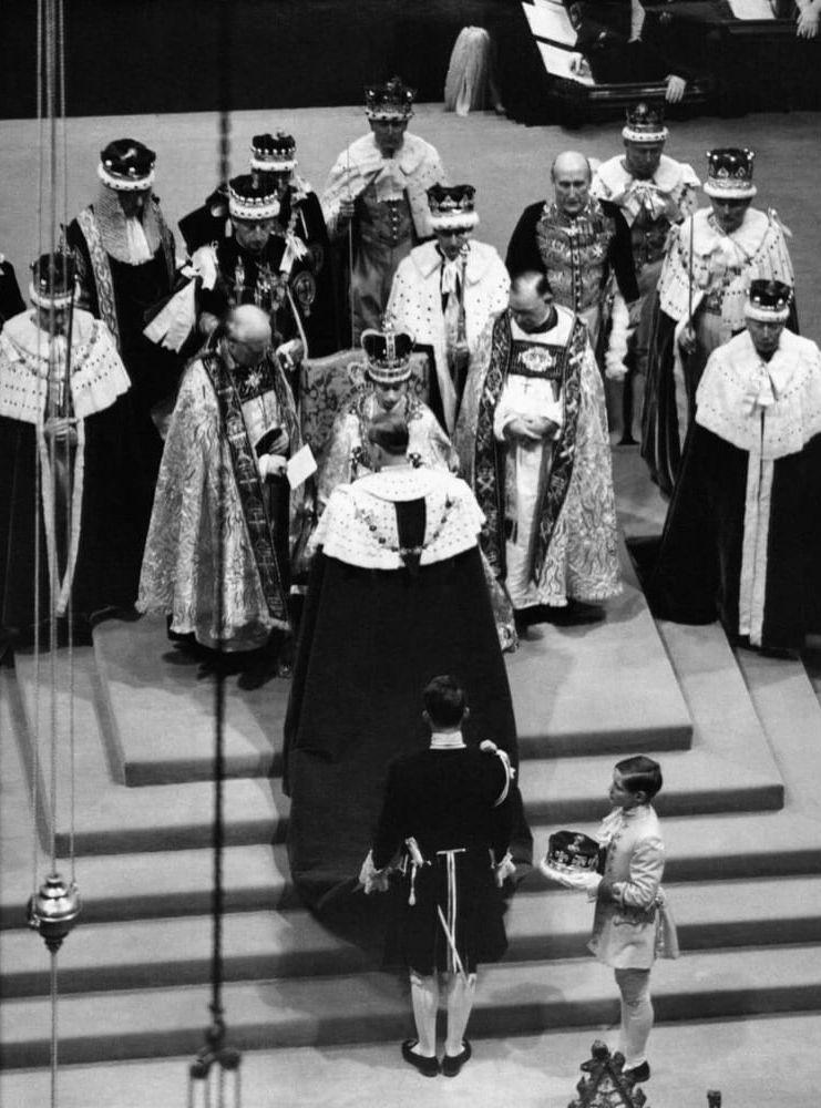Drottningen på sin tron under sin kröning, 1953. Hertigen av Edinburgh, med ryggen mot kameran, hedrar sin fru. Kröningen ägde rum i London den 2 juni 1953.