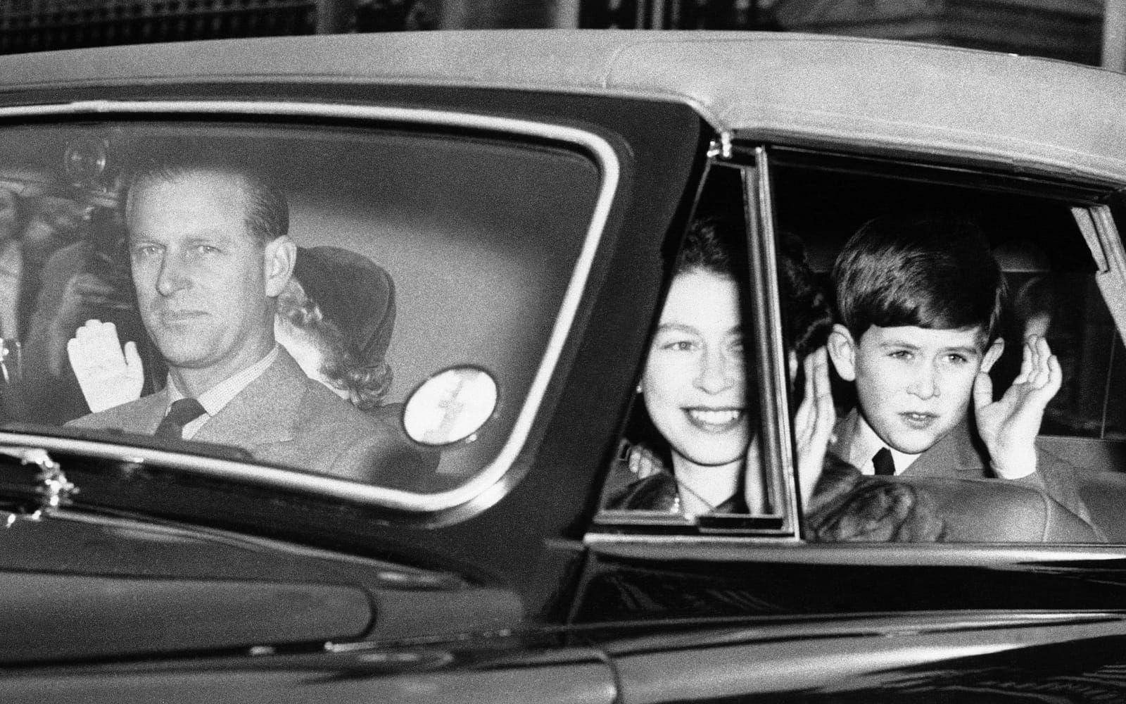 Är man kunglig blir man uppassad även när man ska göra det enklaste ärenden. Här ska familjen åka på picknick och får vinka för kamerorna i mars 1956. Prins Philip håller händerna på ratten när övriga familjen vinkar till dem som ser på.