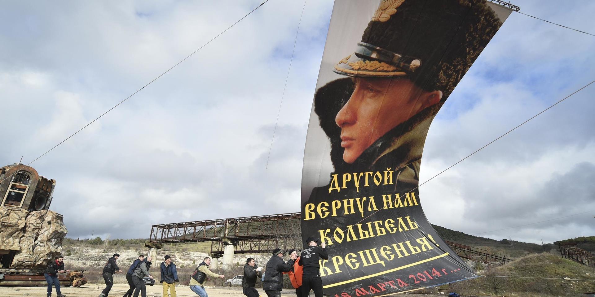 I staden Sevastopol på ukrainska Krimhalvön monteras en flagga med Rysslands president Vladimir Putin, med texten 'En annan gav oss åter dopets vagga', på sjuårsdagen av den ryska annekteringen av Krim i mars i år.