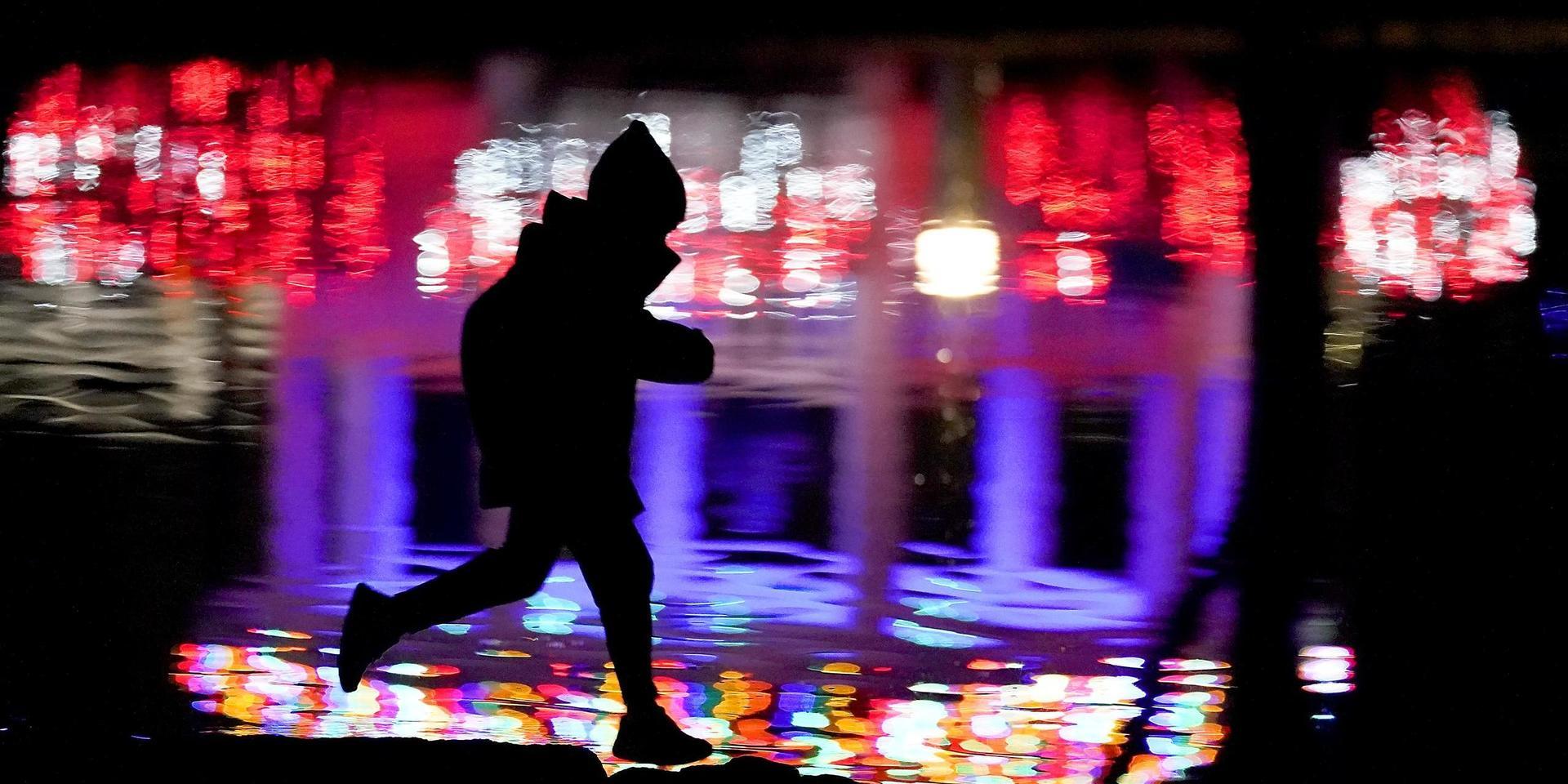 A child is silhouetted against Christmas lights reflected on a pond at a park in Lenexa, Kan., Friday, Dec. 4, 2020. (AP Photo/Charlie Riedel)