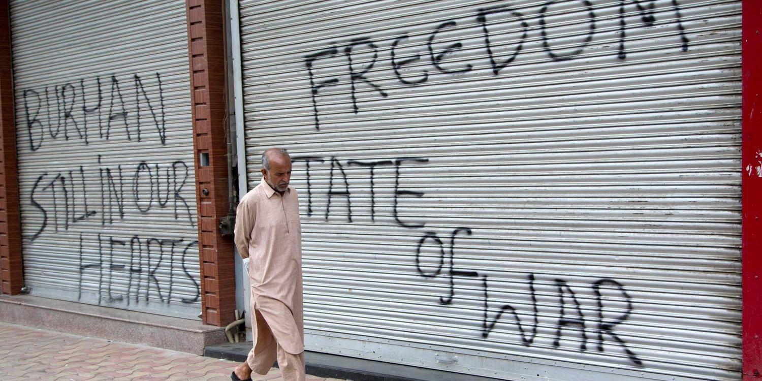 En man går förbi stängda butiker målade med graffiti under utegångsförbudet i Srinagar, i den Indienkontrollerade delen av Kashmir.