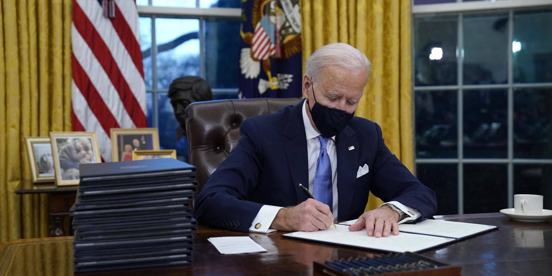 President Joe Biden signs his first executive order in the Oval Office of the White House on Wednesday, Jan. 20, 2021, in Washington. (AP Photo/Evan Vucci)  DCEV554