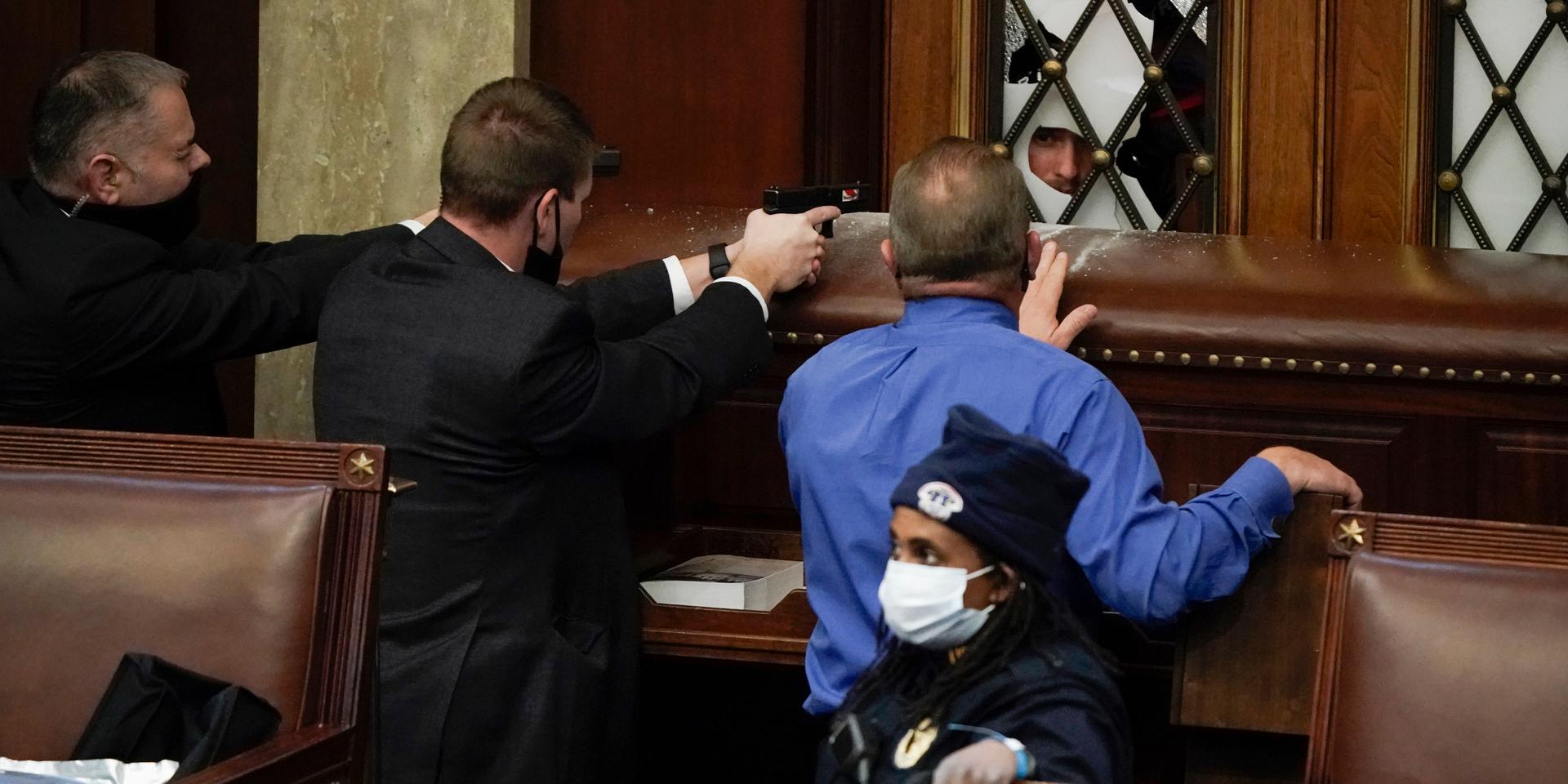 Poliser riktar sina vapen mot upploppsmakare som försöker bryta sig in i kammaren i Kapitolium under stormningen den 6 januari 2021.